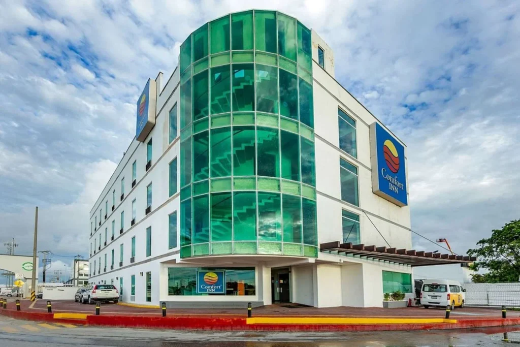 Modern hotel exterior with green glass facade and main entrance at Comfort Inn Cancun Aeropuerto in Cancun