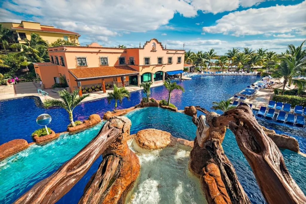Lagoon-style main swimming pool with waterfalls, tropical landscaping, and resort buildings at El Cid Resorts near Cancun, Mexico.