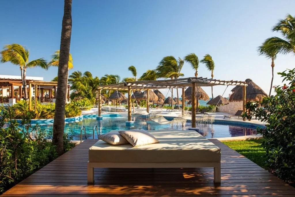 Lagoon-style swimming pool with in-water hammocks, sun loungers, tropical gardens, and palm trees at Excellence Playa Mujeres in Playa Mujeres, Mexico.
