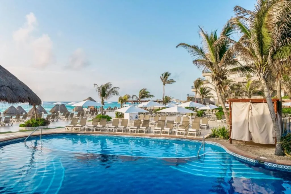 Oceanfront main swimming pool with sun loungers and palm trees at Fiesta Americana Condesa Cancun in Cancún, Mexico.