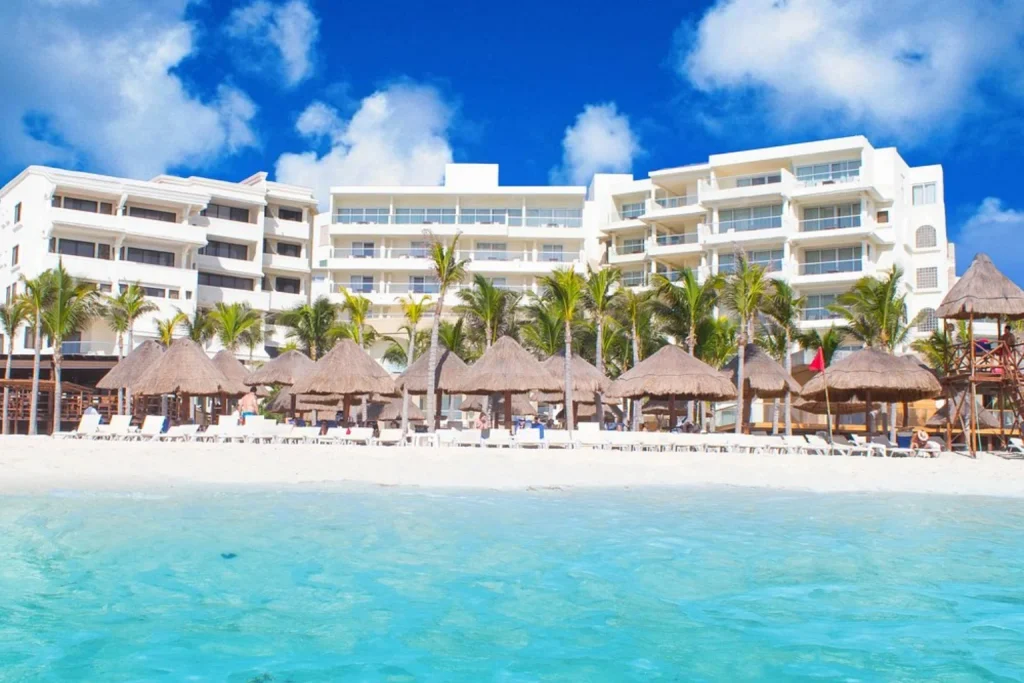 Turquoise Caribbean water, white sandy beach and rows of traditional thatched parasols in front of Hotel NYX Cancun in Cancun.