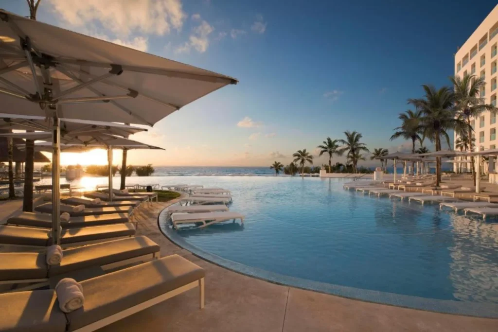 Oceanfront infinity pool with sun loungers at sunset at Le Blanc Spa Resort Cancun – Adults Only in Cancún, Mexico.