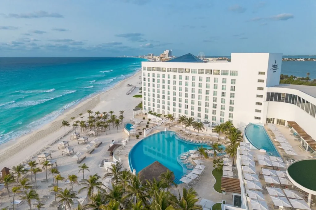 Aerial view of the beachfront infinity pool, white-sand beach, and turquoise Caribbean Sea at Le Blanc Spa Resort Cancun in Cancún, Mexico.