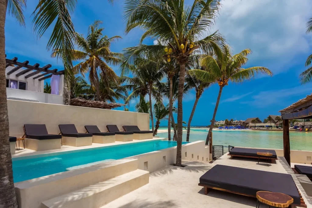 Beachfront infinity-style pool surrounded by palm trees and sun loungers at Lotus Beach Hotel Adults Only on Isla Mujeres near Cancun.