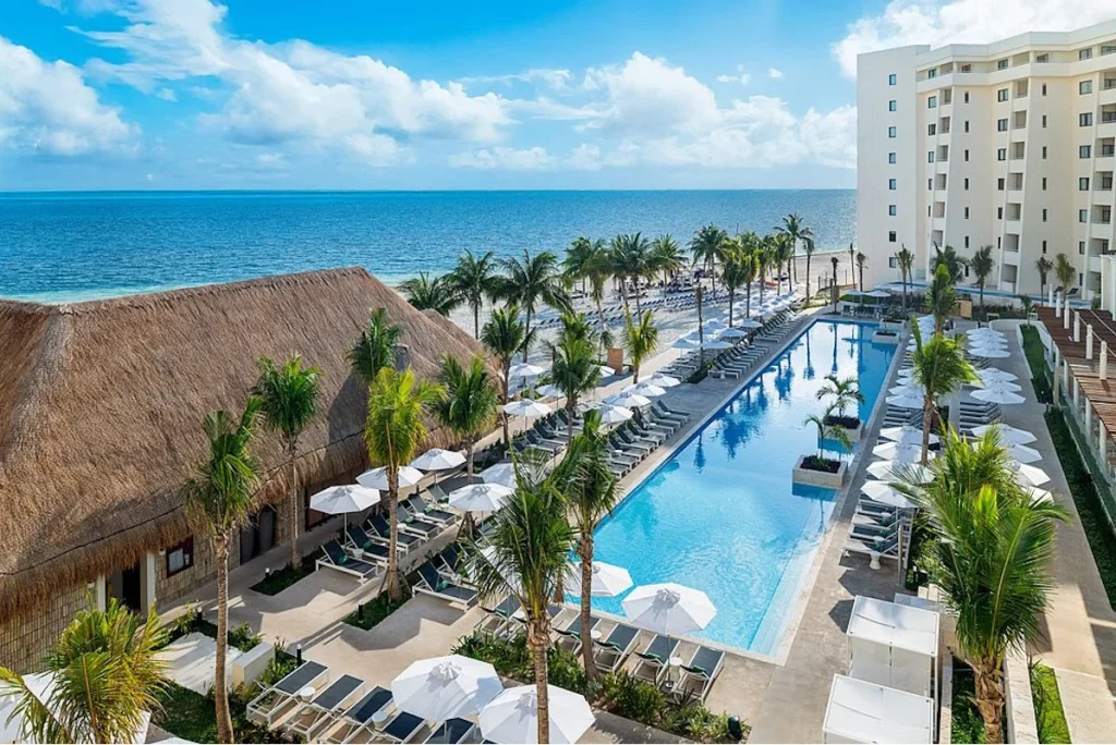 Oceanfront swimming pool lined with palm trees and sun loungers at Meliá Casa Maya Cancún in Cancún.