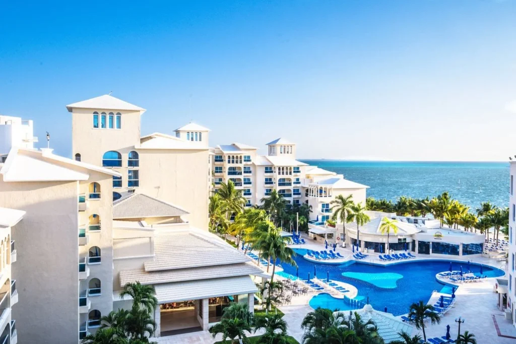 Outdoor swimming pool surrounded by palm trees with the Caribbean Sea in the background at Occidental Costa Cancún in Cancun
