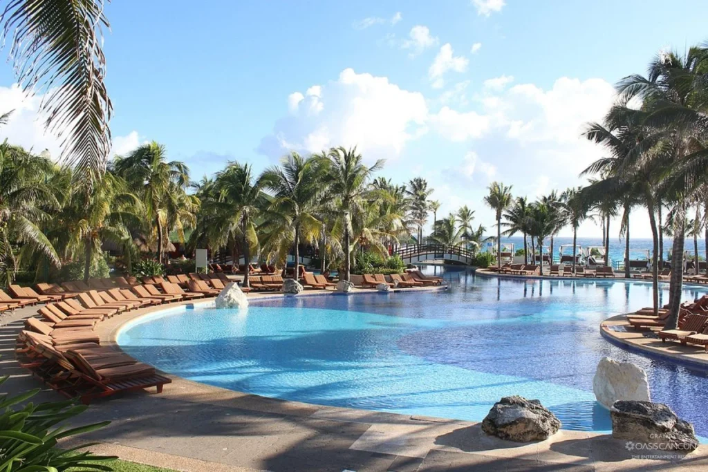 Large tropical outdoor swimming pool surrounded by palm trees and sun loungers, Grand Oasis Cancun