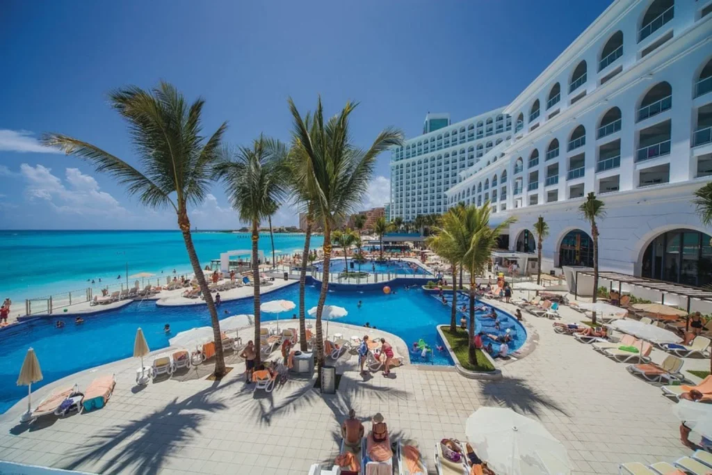 Beachfront swimming pool with palm trees and Caribbean Sea view at Riu Cancun in Cancun