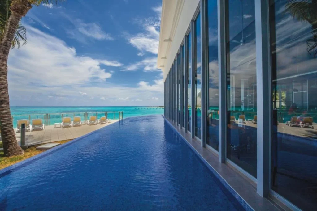 Infinity pool overlooking the turquoise Caribbean Sea with sun loungers and oceanfront terrace at Riu Cancun in Cancún, Mexico.
